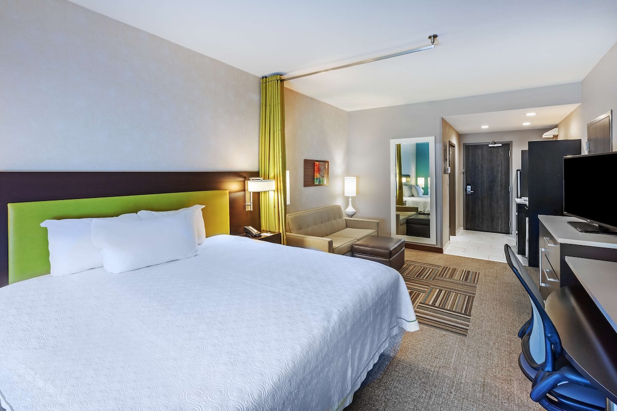 Une chambre d’hôtel avec un grand lit, un bureau avec une chaise, une télévision et une salle de bain visible à travers une porte ouverte.