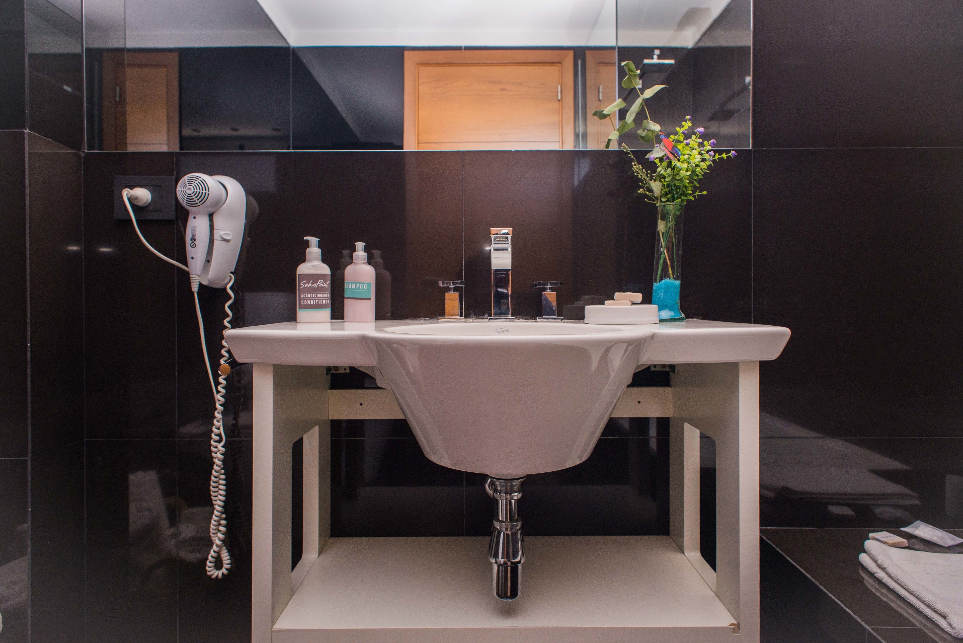 Une salle de bain moderne avec un lavabo blanc, un sèche-cheveux et des articles de toilette.