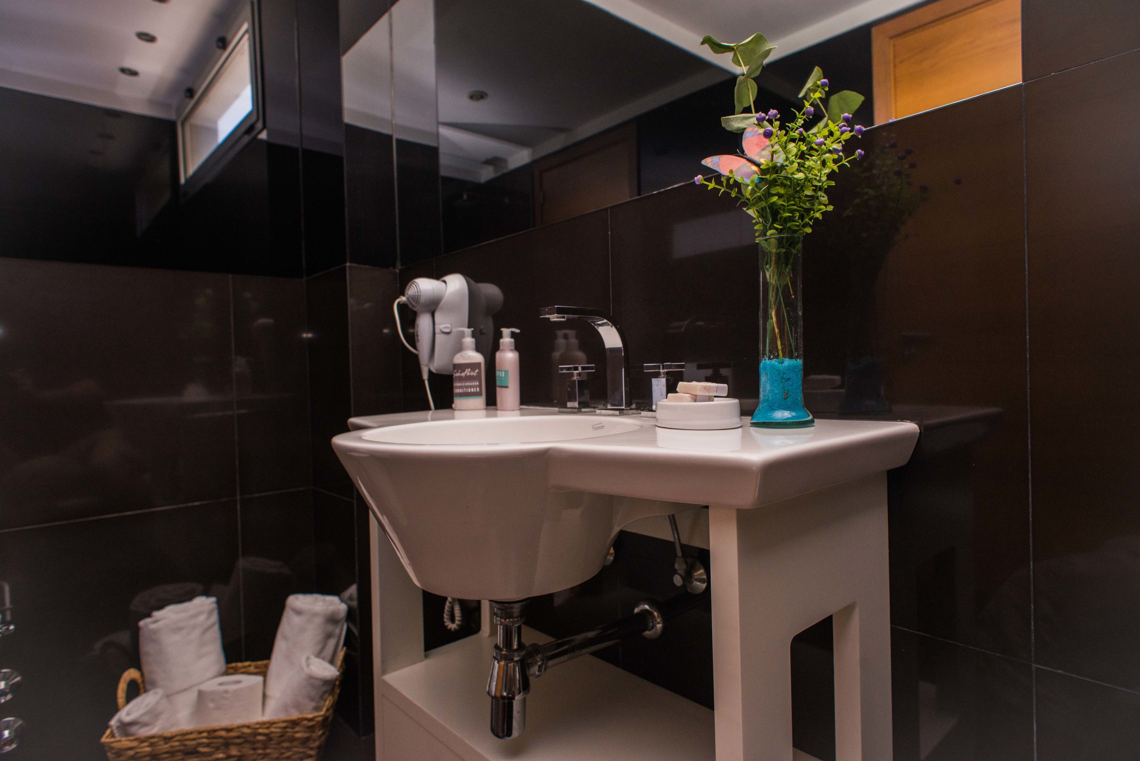 A modern bathroom with a white sink, a hairdryer, and a vase with flowers.
