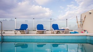 Ein Swimmingpool mit drei blauen Liegestühlen und einer weißen Wand mit Bambusdekor.