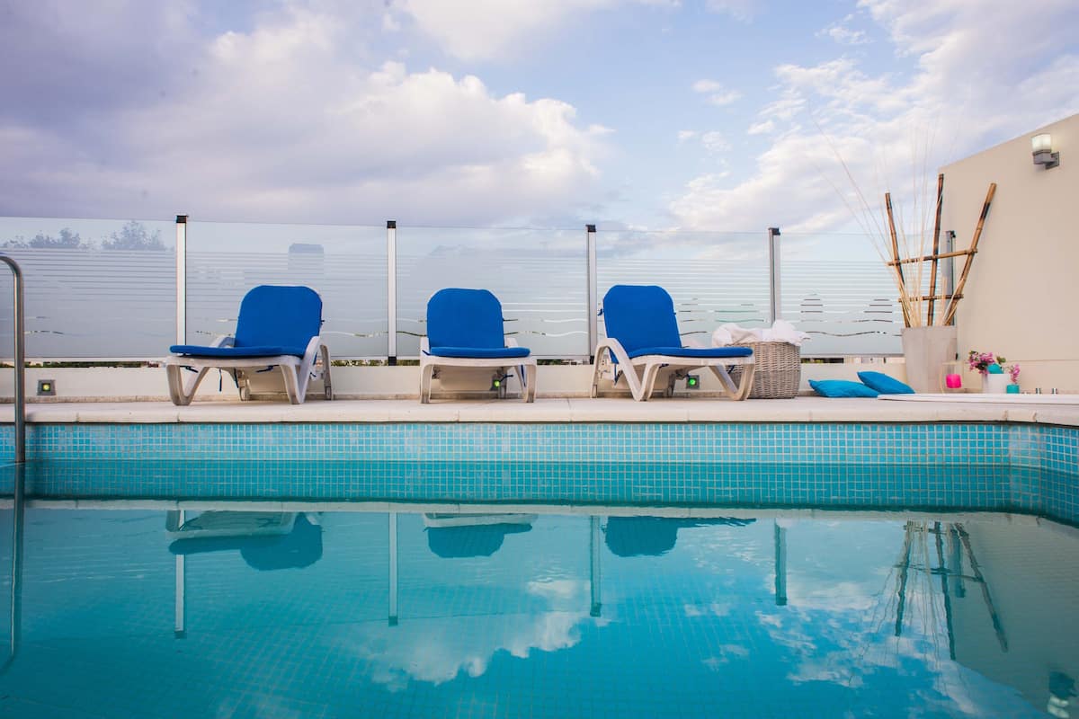 Una piscina con tres sillones reclinables azules y una pared blanca decorada con bambú.