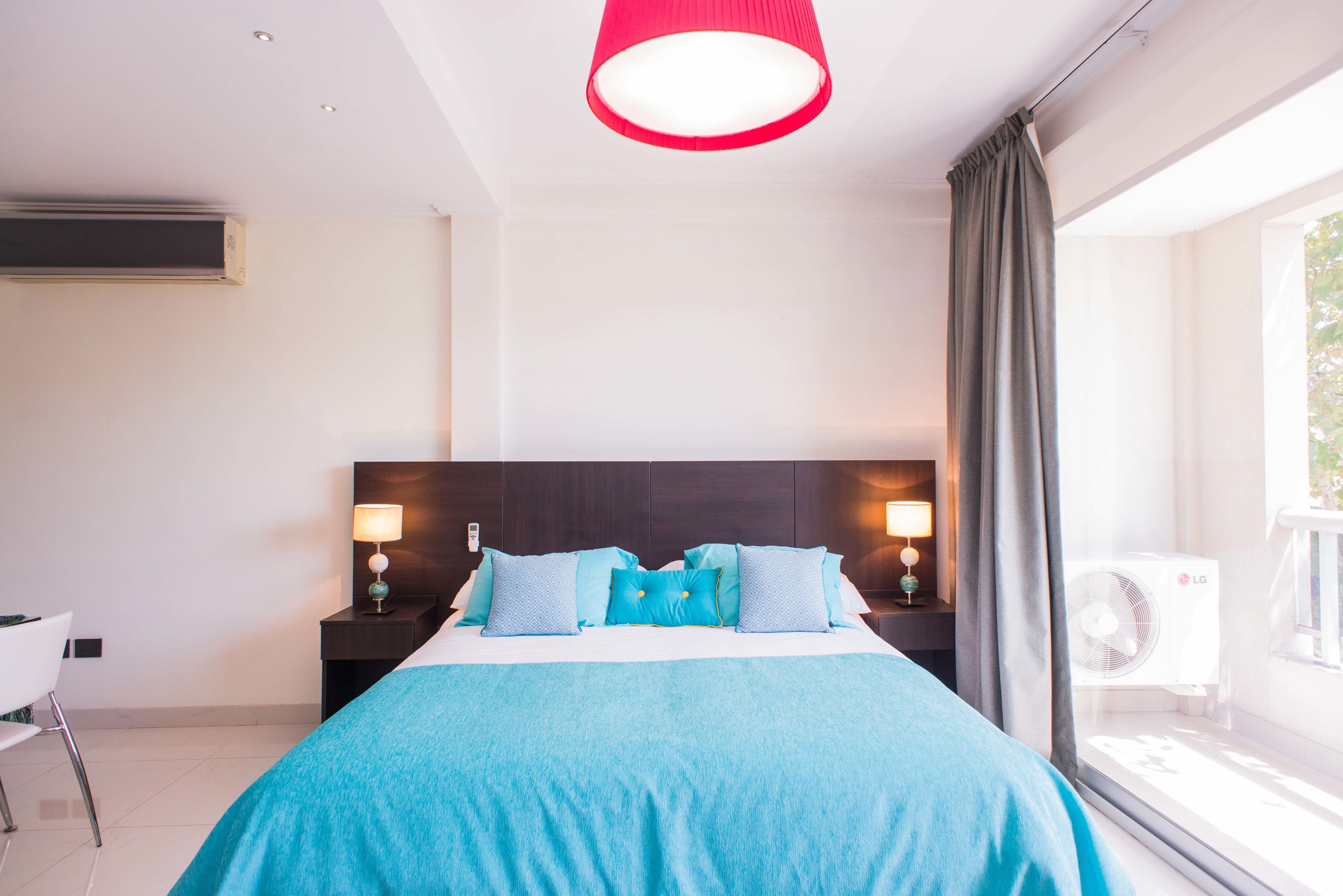 Ein Hotelzimmer mit einem großen Bett, zwei Nachttischen inklusive Lampen, einem Fenster mit Vorhängen und Blick ins Freie.