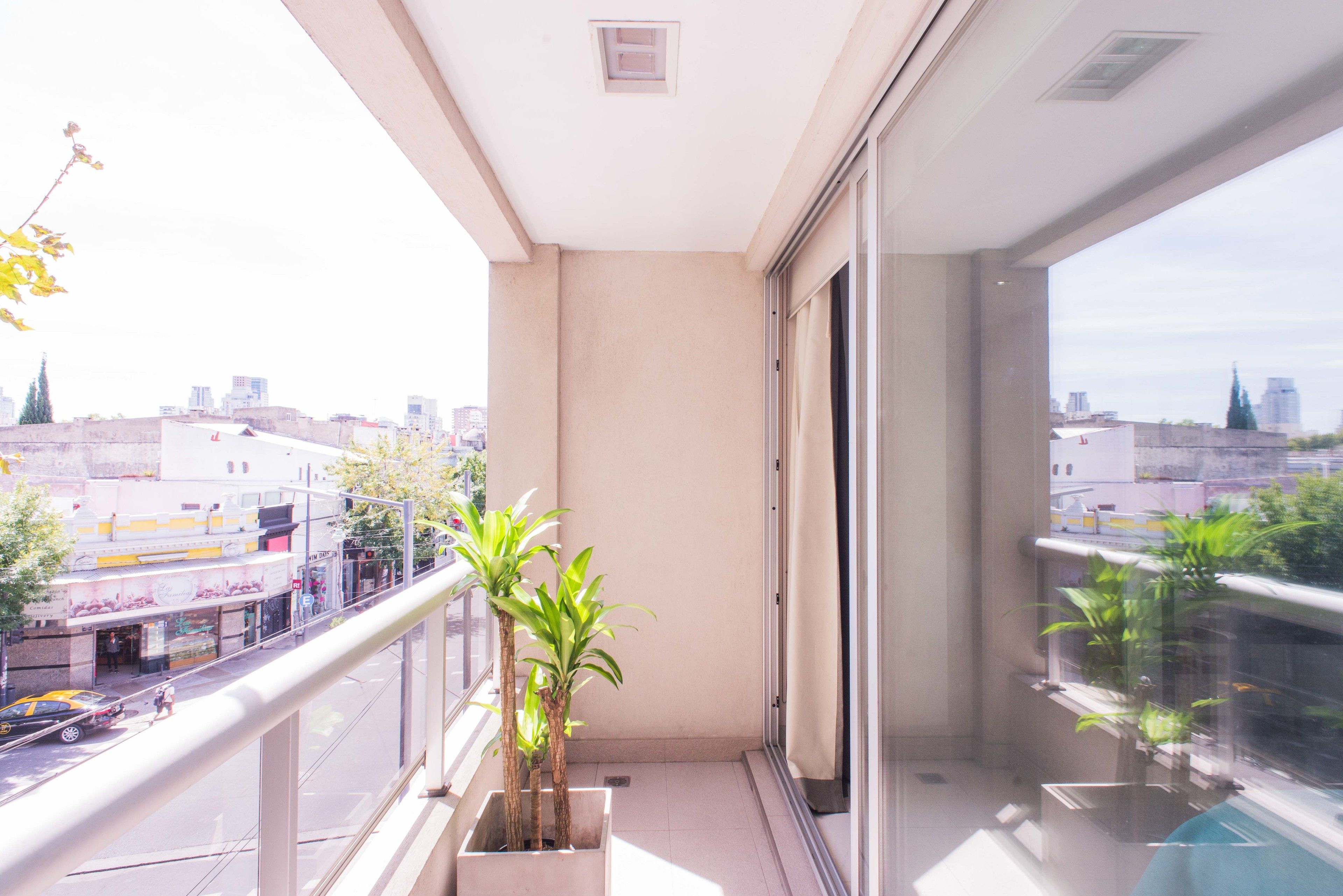 Un balcón con vistas a la ciudad, plantas en macetas y un ventanal que da a un espacio interior.