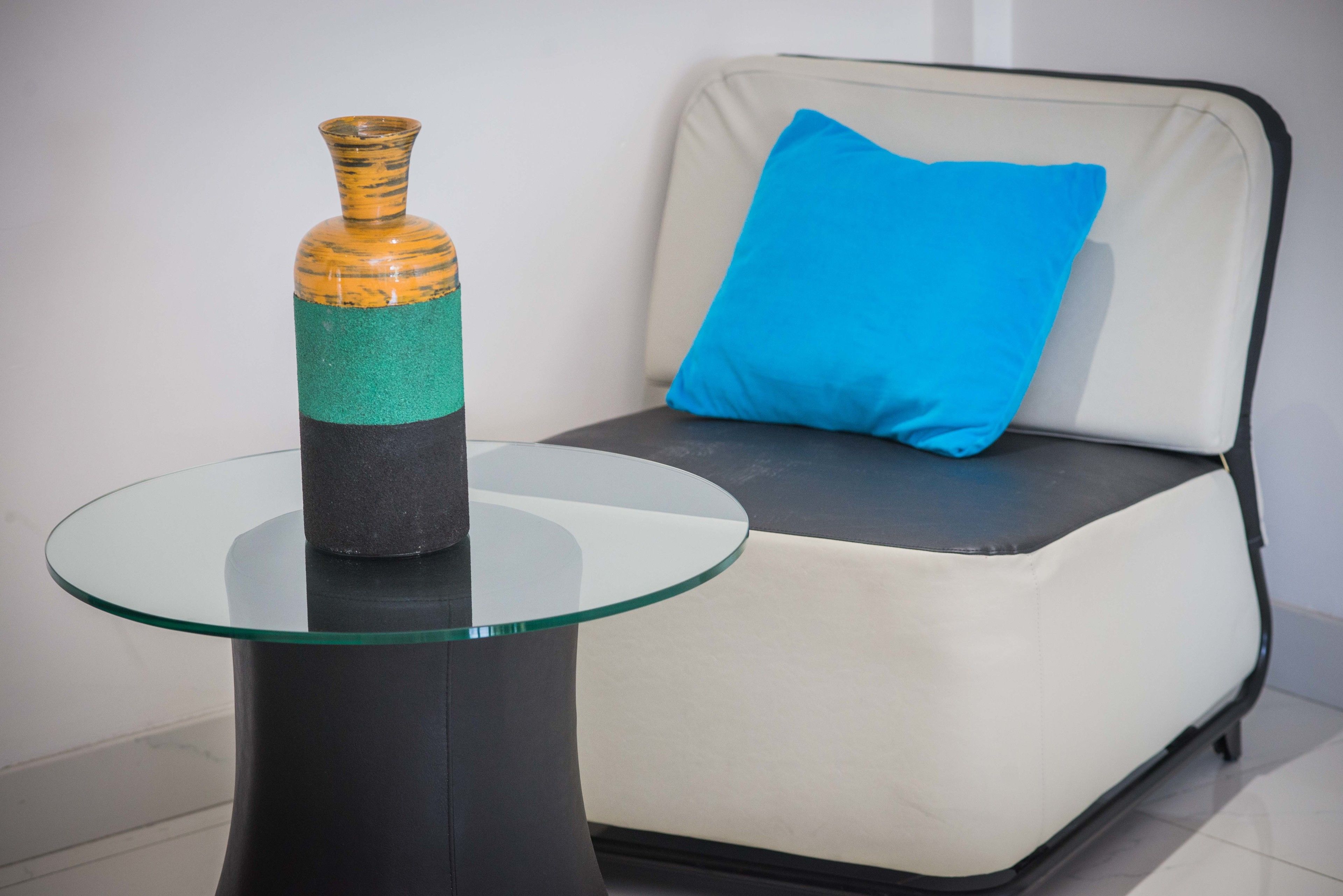Un tavolino in vetro con un vaso e un cuscino blu su un divano.
