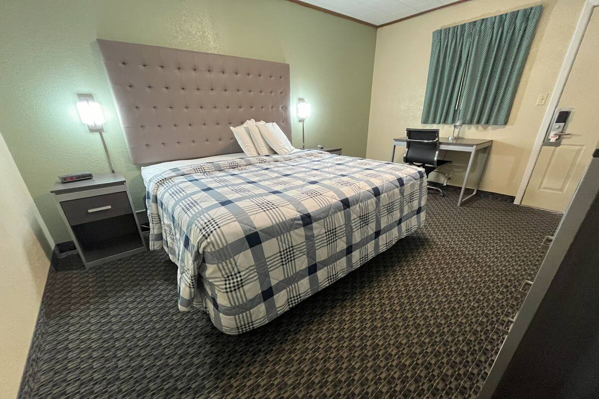 A hotel room with a bed, a desk, a chair, a nightstand, and a lamp.
