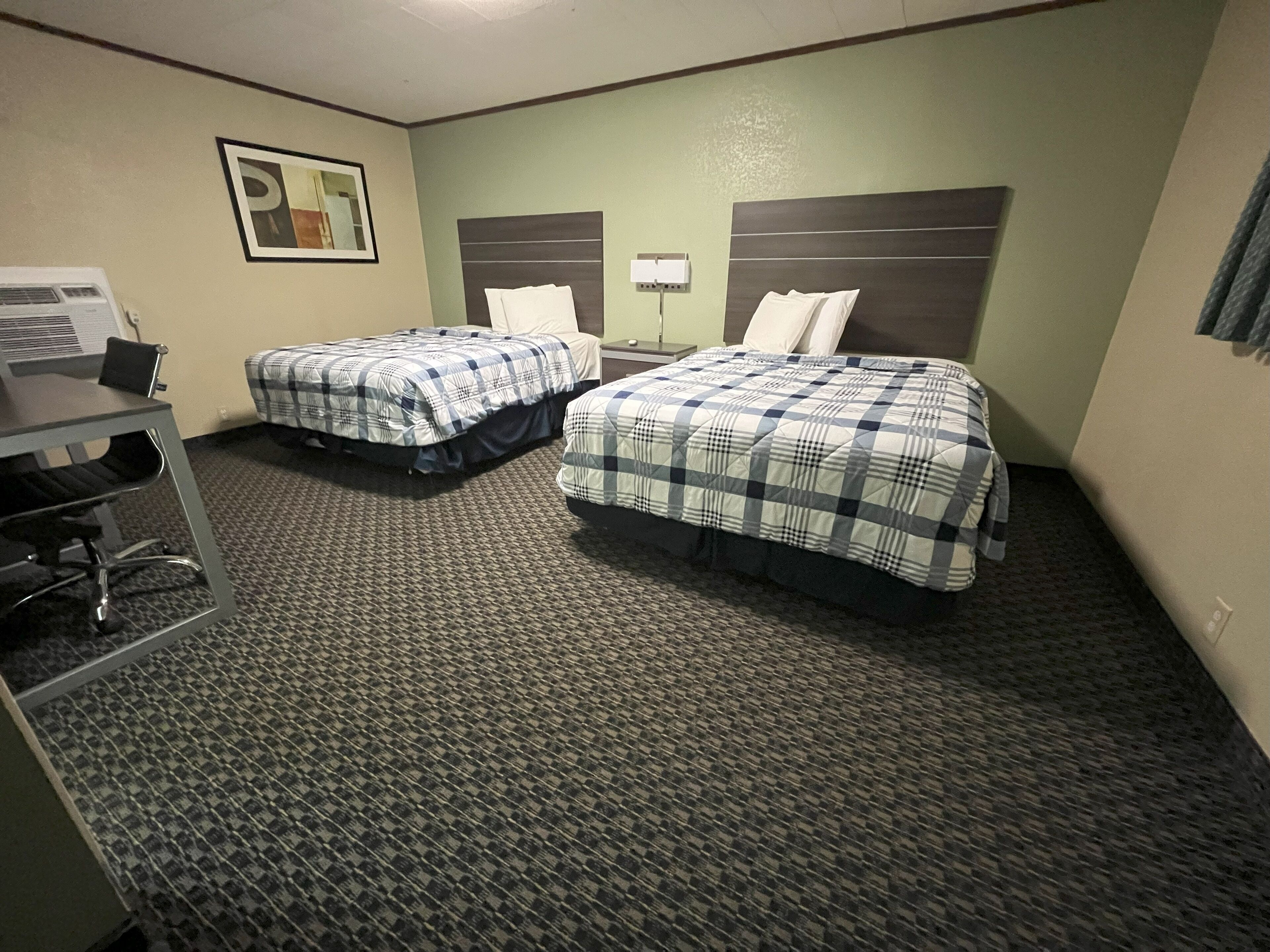 A hotel room with two beds, a desk, and a chair.