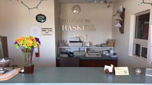 A reception desk with a 'Welcome to Haskill Inn' sign, a vase of flowers, and a 'No Smoking' sign.