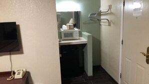 A narrow hallway with a microwave on a counter, a trash bin, a telephone, and a coat rack with hangers.