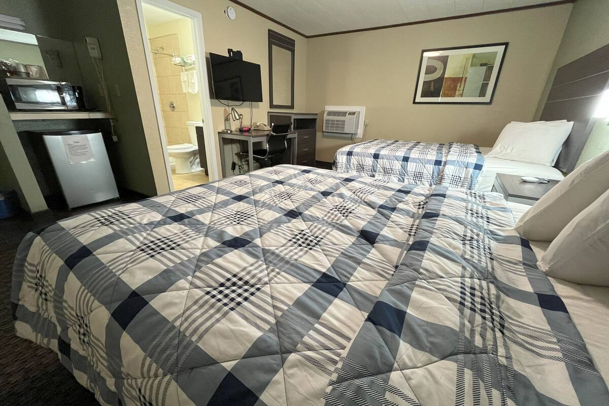 A hotel room with a large bed, a desk with a computer, a TV, and a kitchenette area.