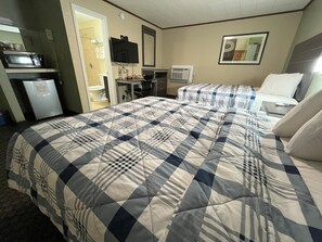 A hotel room with a large bed, a desk with a computer, a TV, and a kitchenette area.