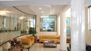 Un hall d’entrée moderne avec un comptoir de réception en verre, un canapé jaune, une table basse et une grande fenêtre donnant sur un magasin.