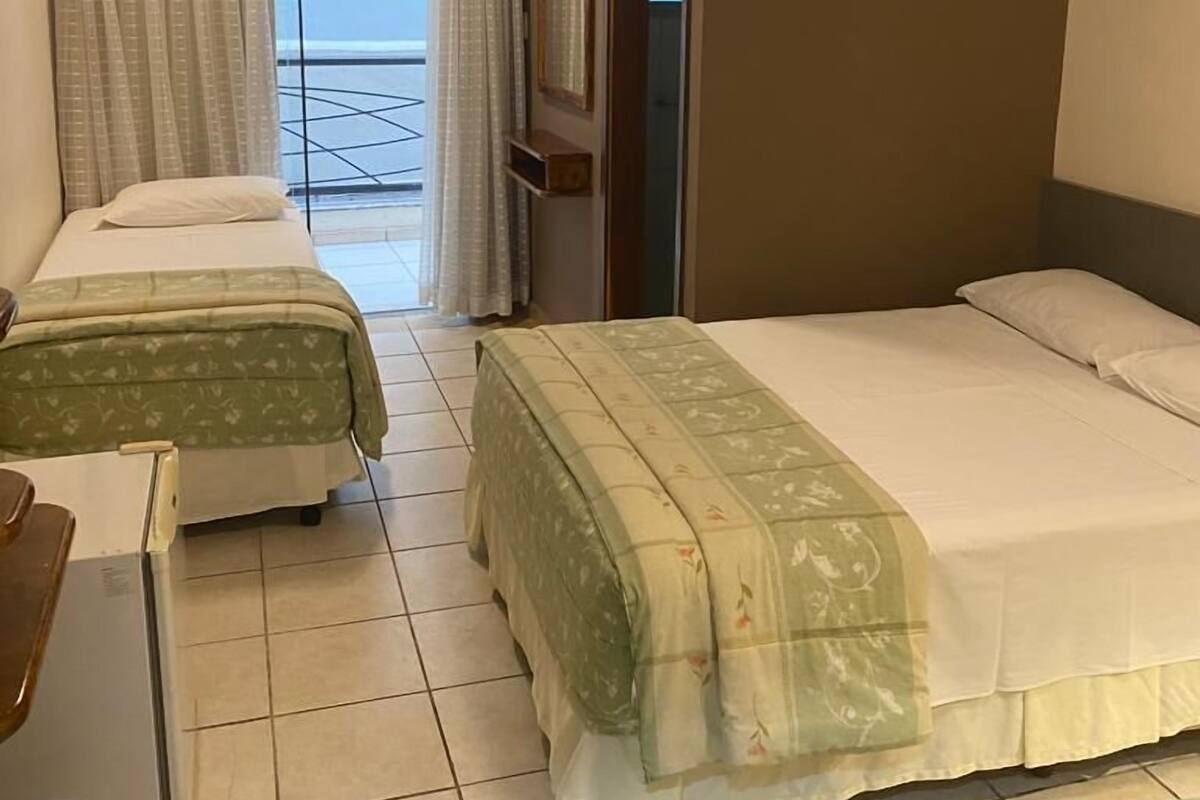 A hotel room with two beds, a desk, and a view of the sea.