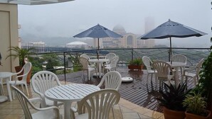 Un espace extérieur abrité, avec des chaises et des tables en plastique blanc, des parasols et des plantes en pot.