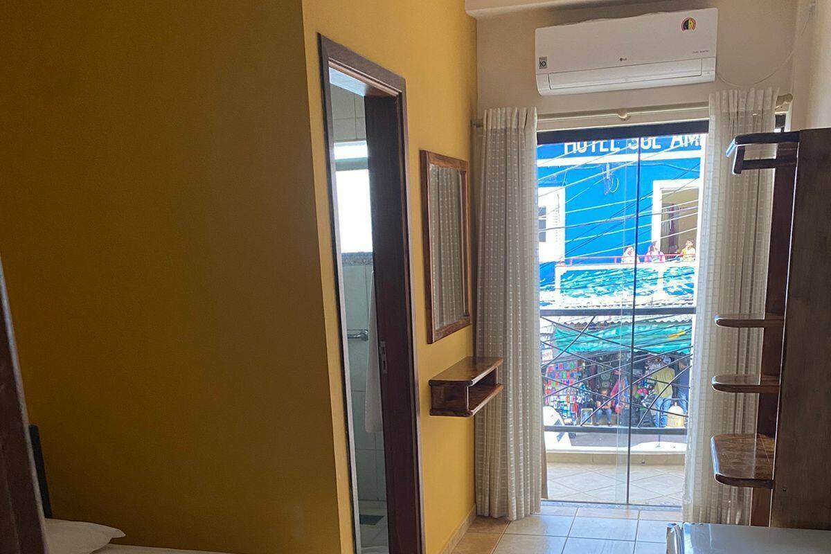 A hotel room with a bed, a small desk, a wardrobe, and a view of a bustling street outside.