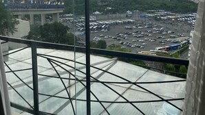 Vue depuis un balcon doté d’une balustrade en verre, donnant sur un parking et des bâtiments situés au loin.
