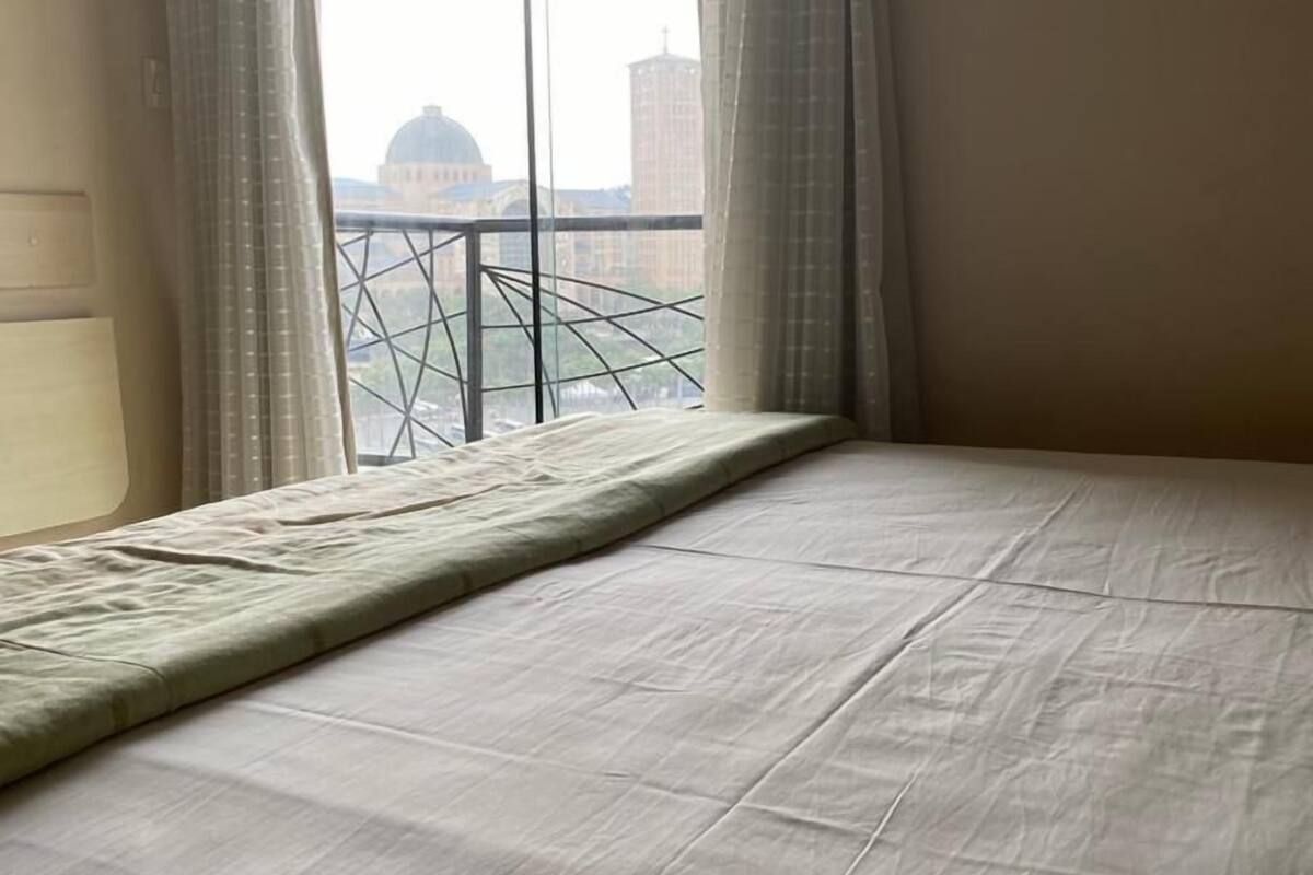 A hotel room with a bed, a window with curtains, and a view of a cityscape including a dome and a tall building.