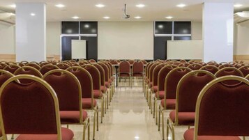 Un salón de conferencias con filas de sillas rojas y una pizarra blanca al frente.