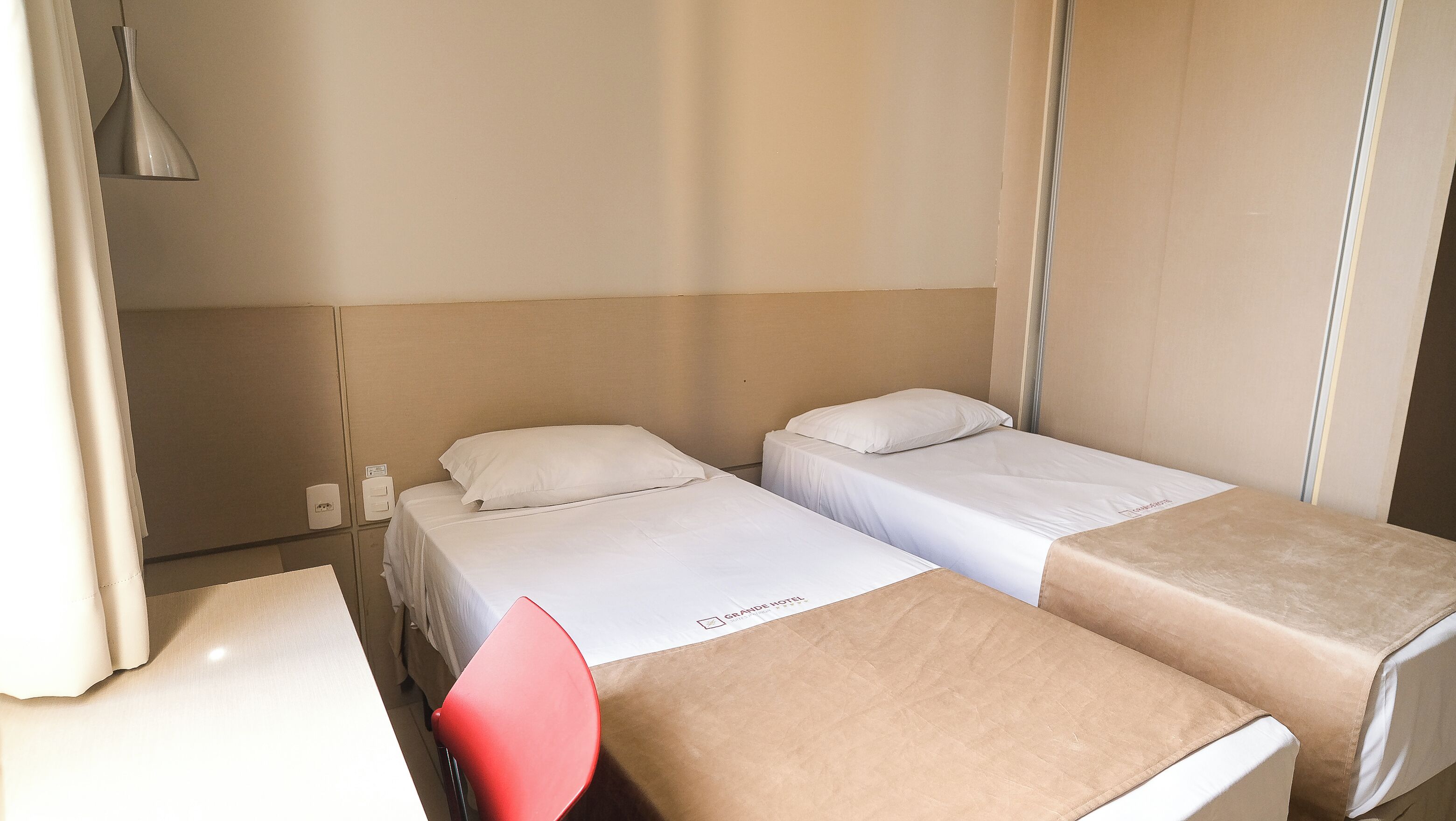 A hotel room with two beds, a red chair, and a small table.