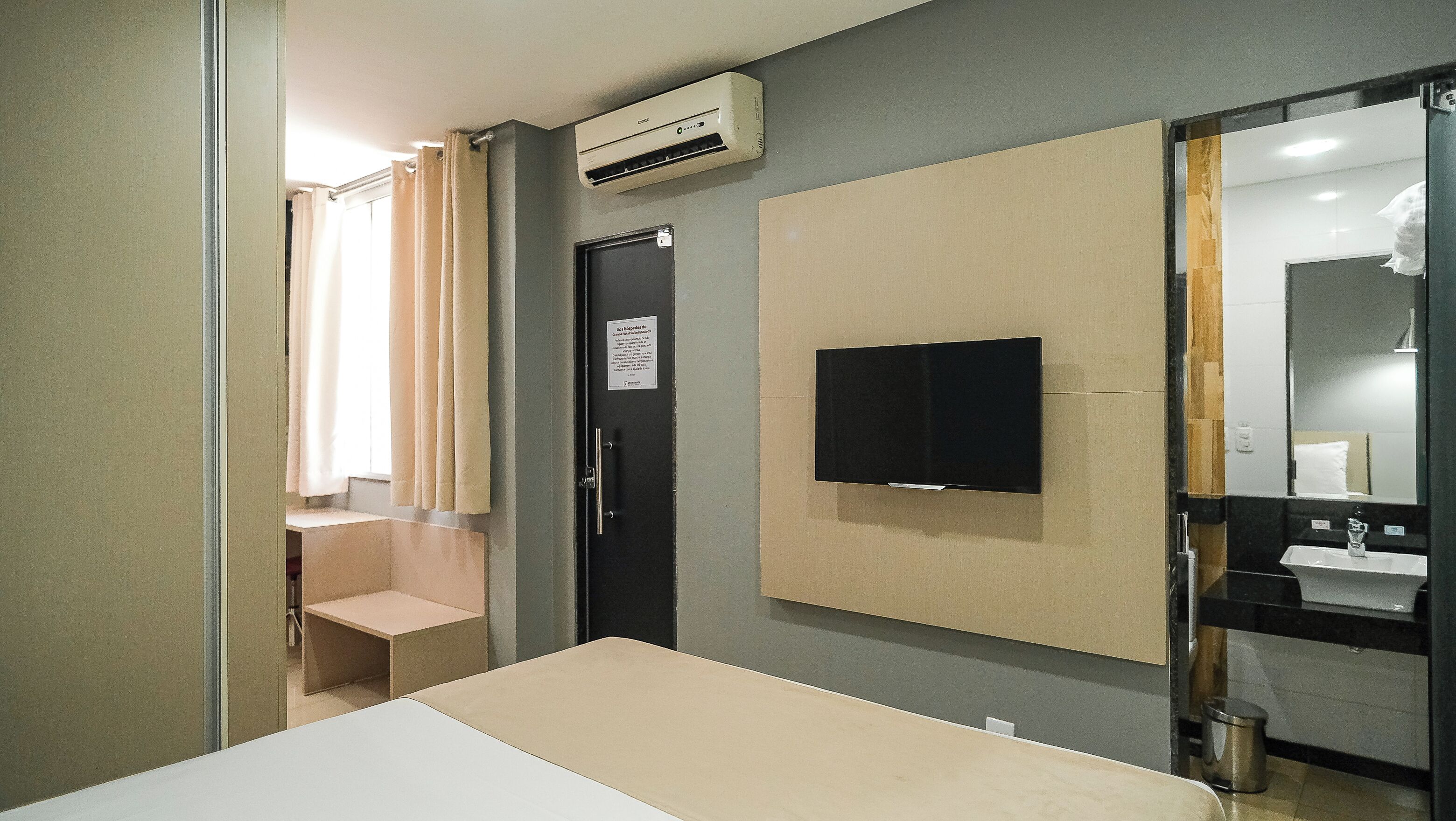 Quarto de hotel com uma cama, televisão fixada na parede, pia e espelho.