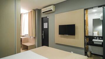 Quarto de hotel com uma cama, televisão fixada na parede, pia e espelho.