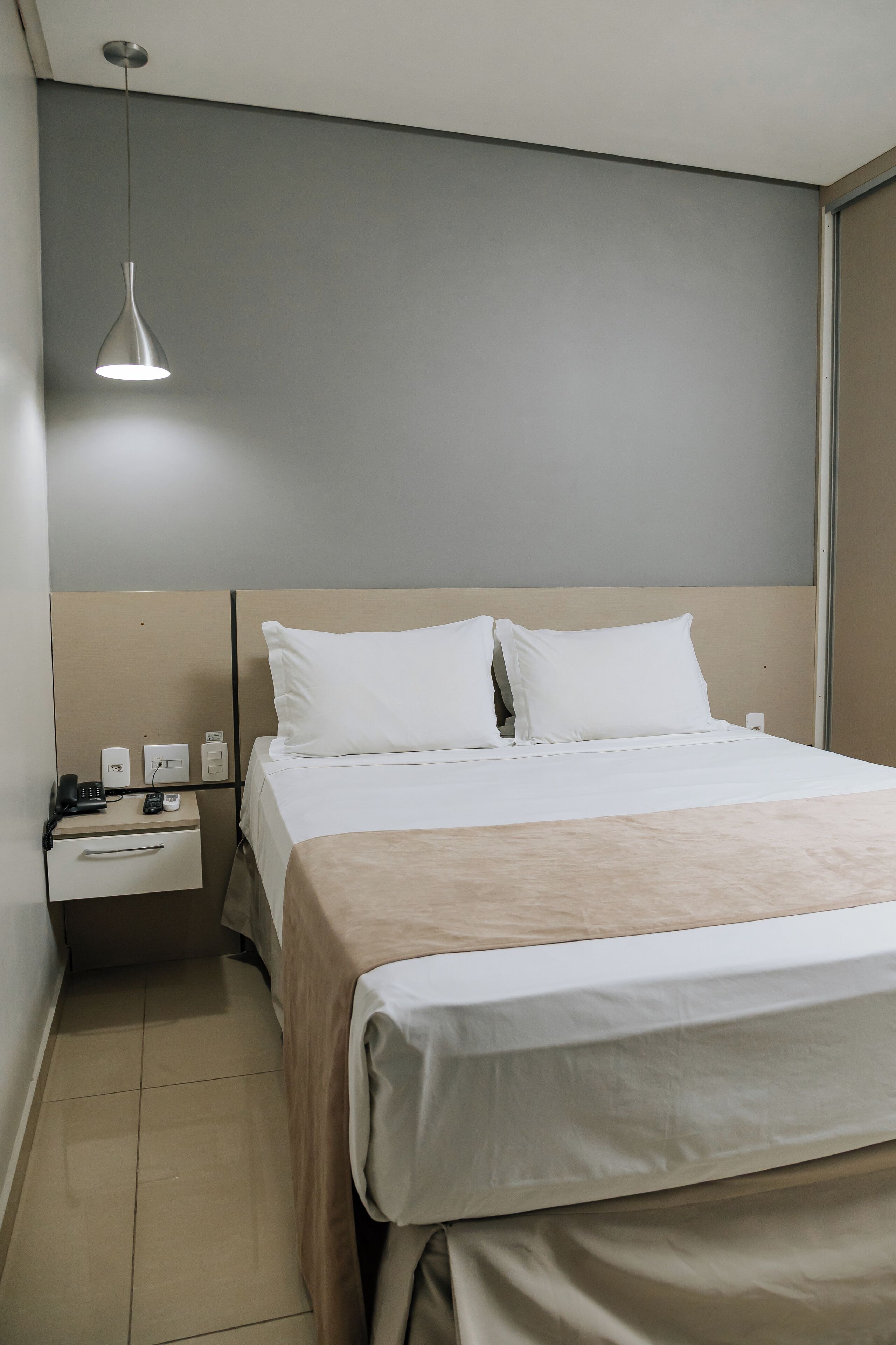 A hotel room with a bed, bedside table, lamp, and a power outlet.