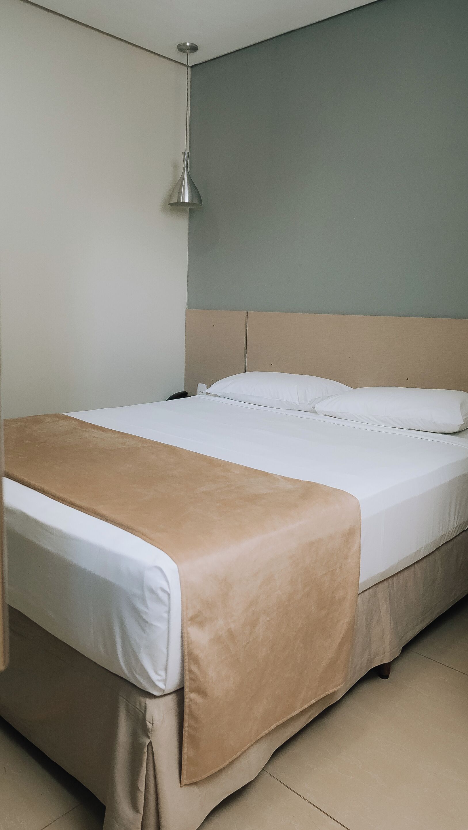 A single bed with a beige bedspread, a white pillow, and a headboard against a grey wall.
