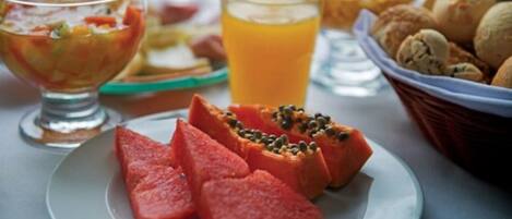 Ein Frühstücksbuffet mit Wassermelone, einem Glas Orangensaft und einer Schüssel Obstsalat.