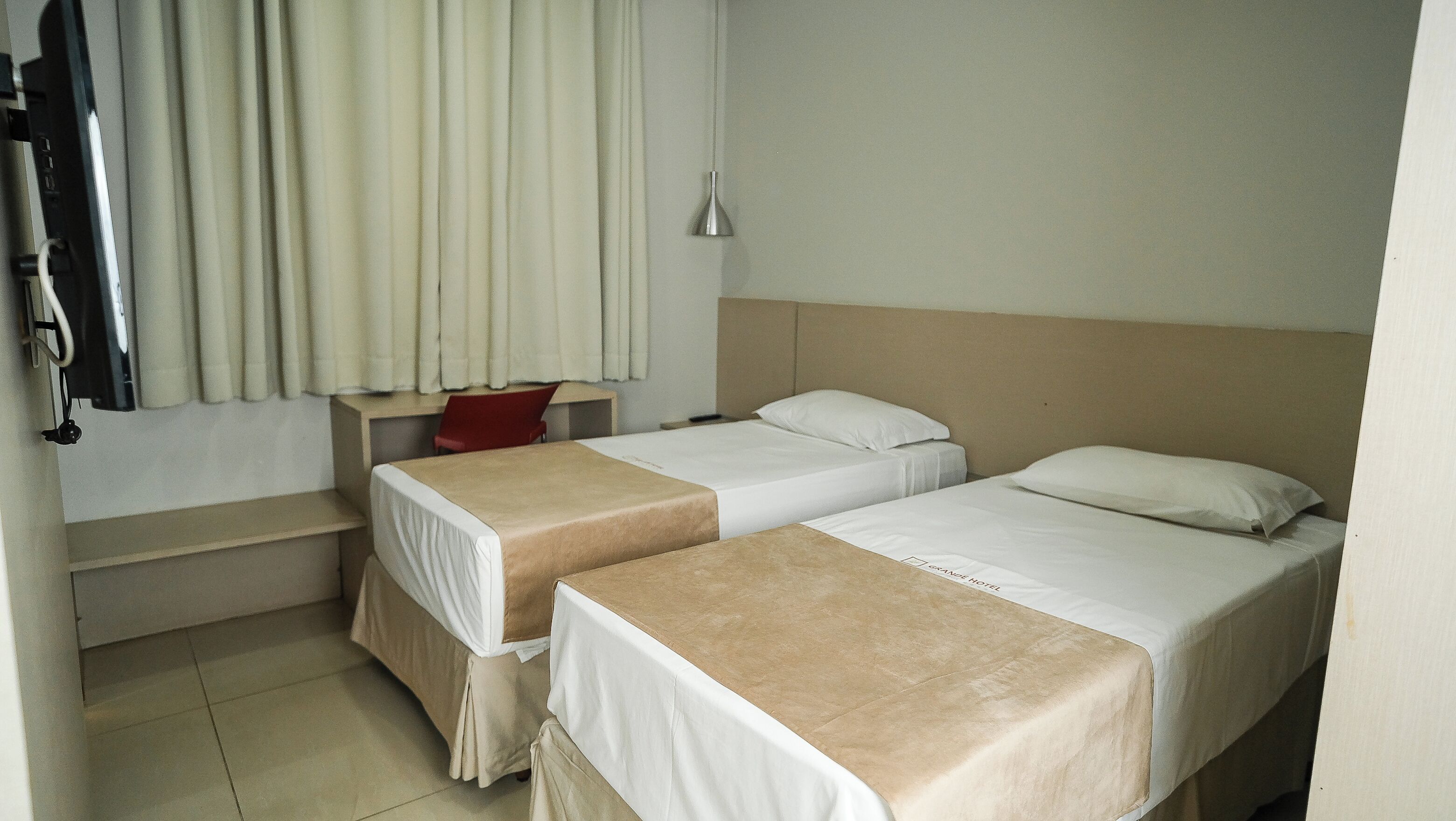 Habitación de hotel con dos camas, un escritorio, una silla, una lámpara colgante y una cámara de seguridad.