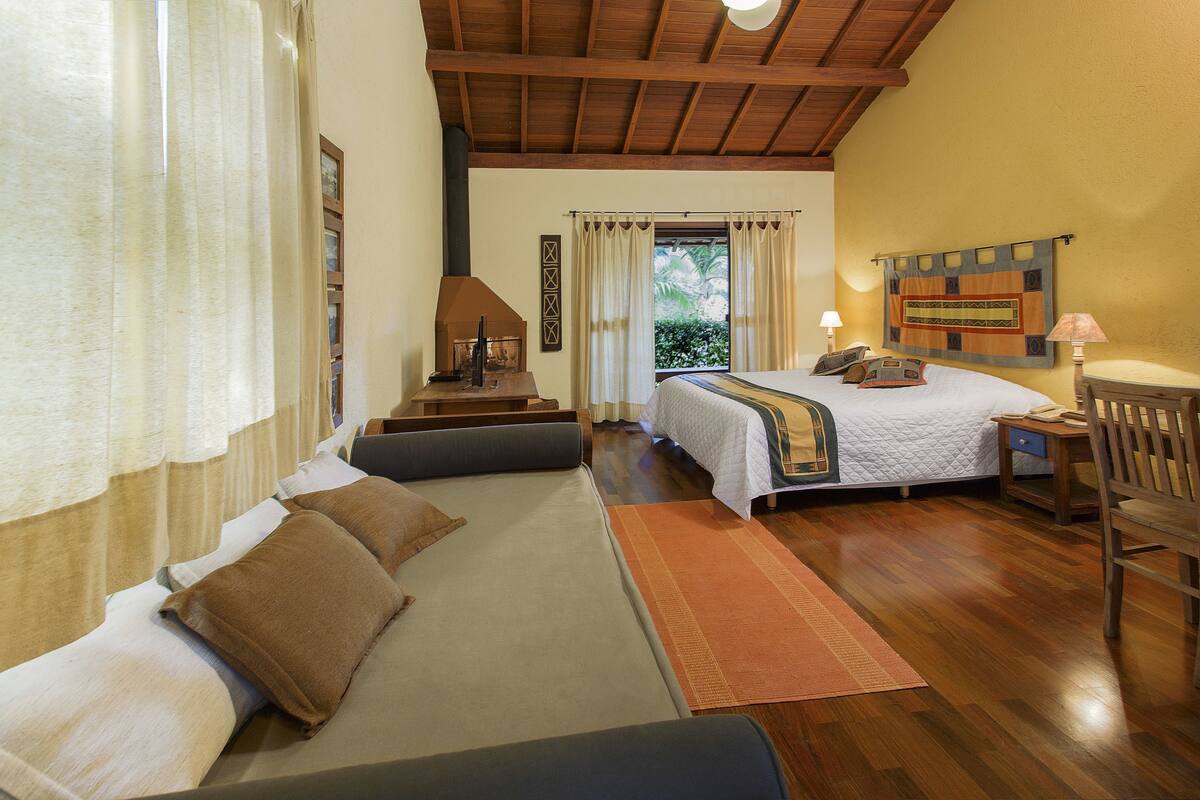 A cozy bedroom with a bed, a sofa, a desk, and a guitar.