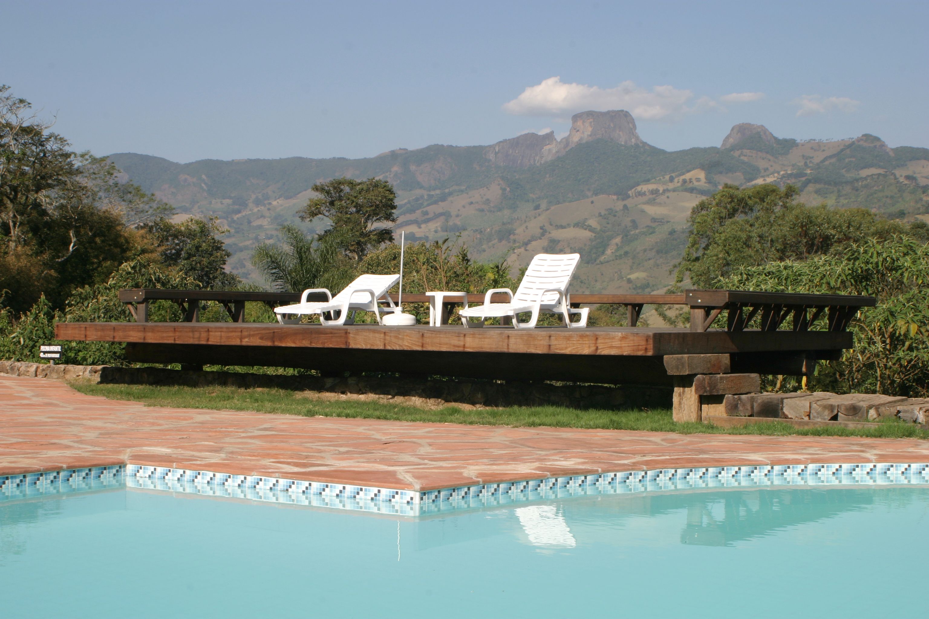 A pool with white lounge chairs and a wooden deck overlooking a mountainous landscape.