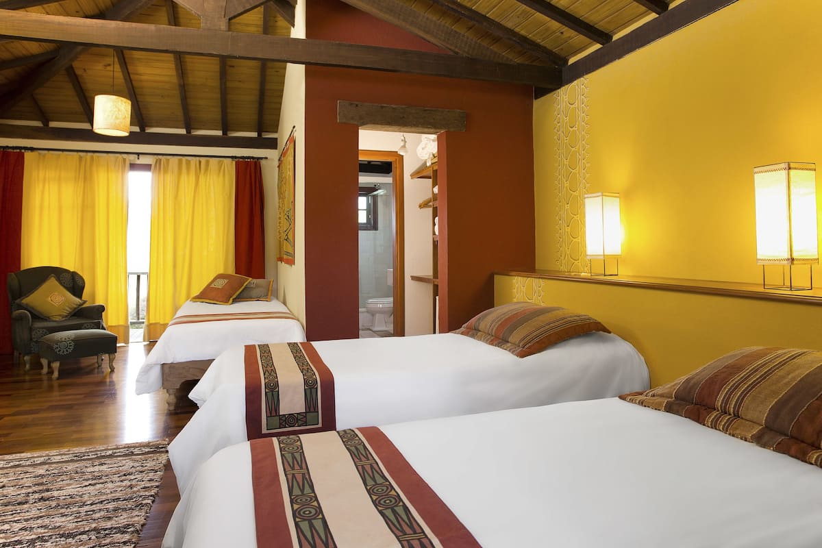 A hotel room with three beds, a wooden ceiling, and a yellow wall.