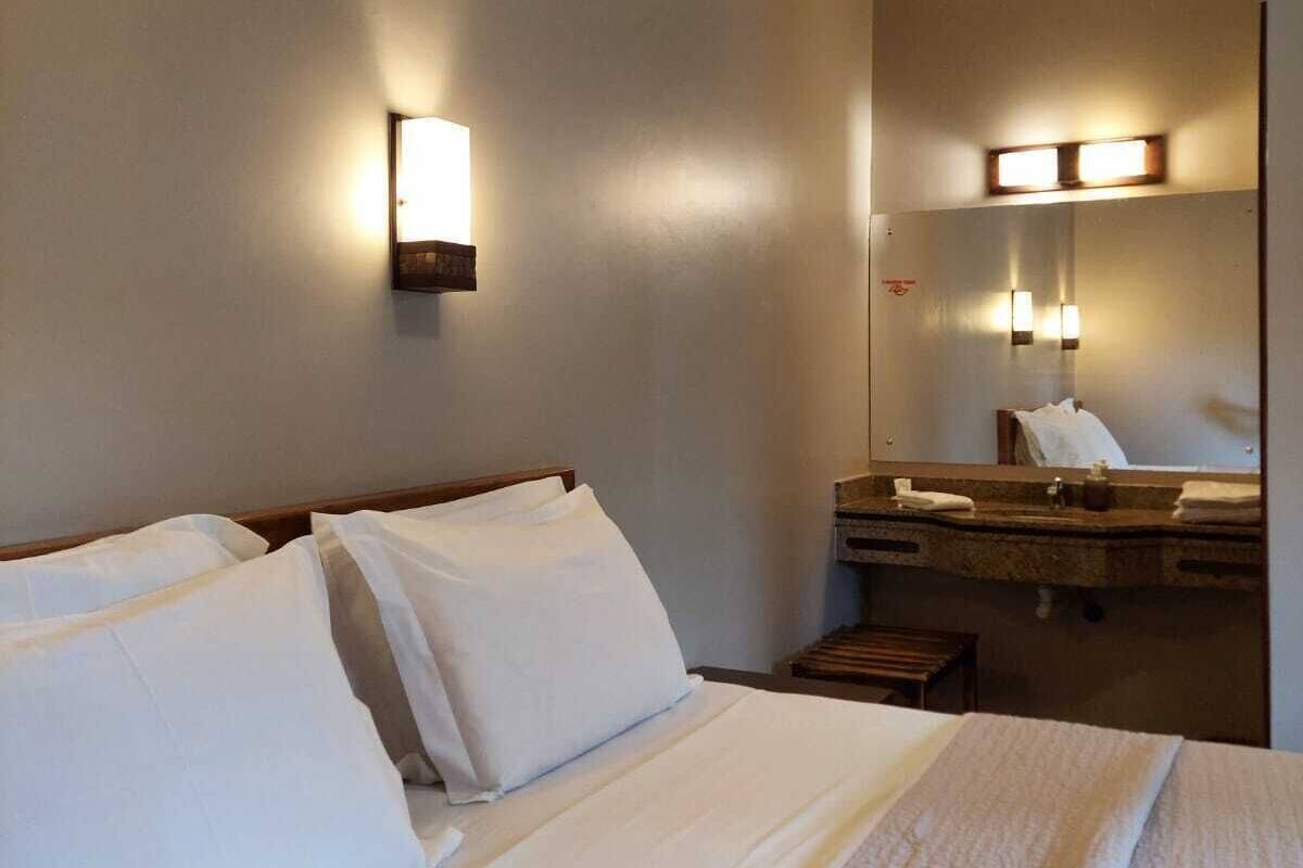 Una habitación de hotel con una cama, una mesita de noche, un espejo e iluminación en la pared.