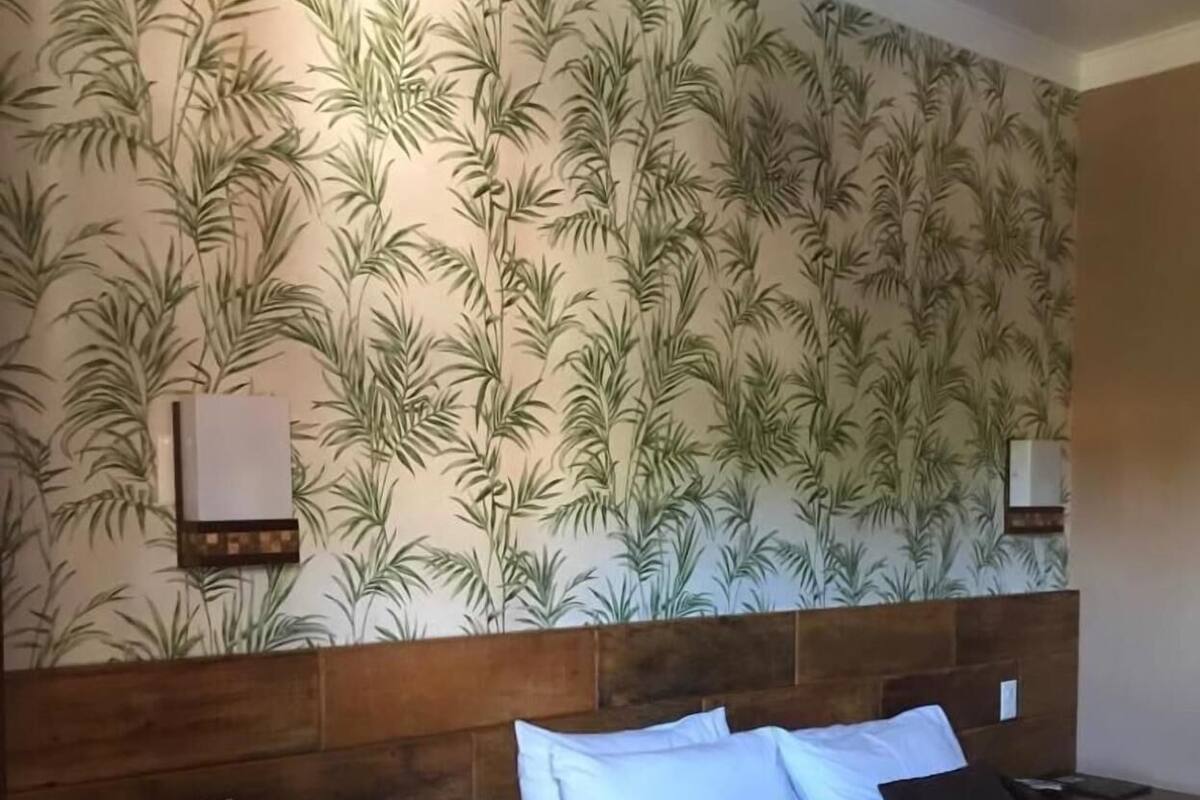 Habitación de hotel con cama, cabecera de madera y una pared con diseño de hojas.
