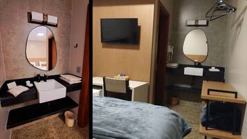 Habitación de hotel con un espejo redondo, un televisor de pantalla plana, un escritorio y una cama con manta azul.