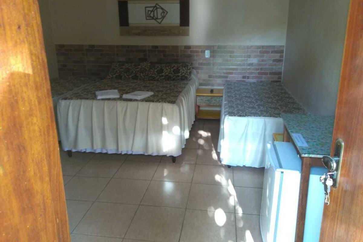 A small, well-lit room with a bed, a small table, and a refrigerator.