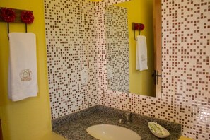 Un baño con una pared amarilla, un lavamanos con encimera de granito y un espejo con un reverso de mosaico.