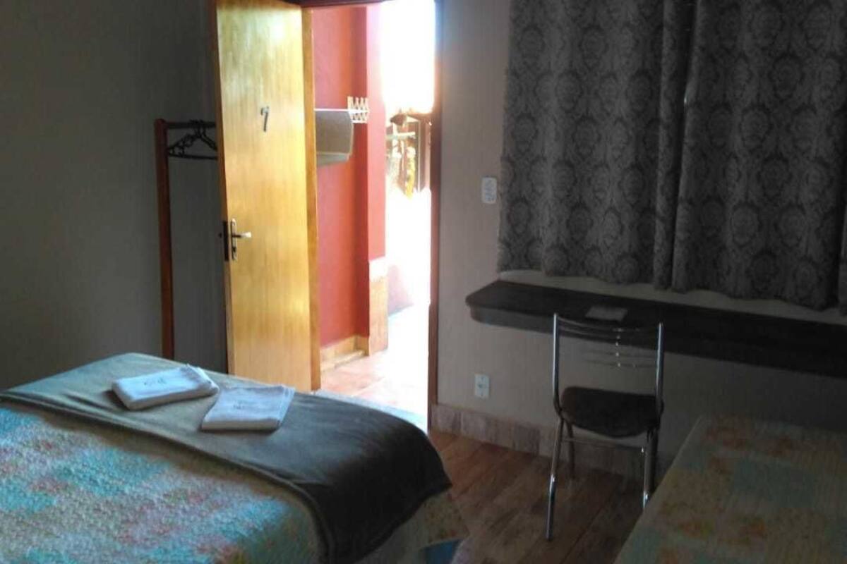 A bedroom with a bed, a desk, and a chair. There is a door leading to another room.