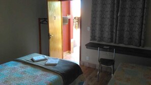 Un dormitorio con una cama, un escritorio y una silla. Hay una puerta que da a otra habitación.