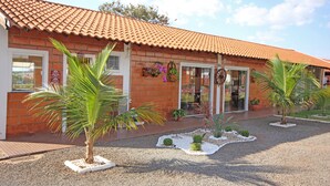 Un bâtiment doté d’un toit en tuiles, d’une façade en briques et d’un petit jardin agrémenté de palmiers et de plantes en pot.