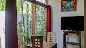 A room with a wooden dining table and chairs, a TV on a stand, and large windows with red curtains. - Résidence Marina Beach (Nouméa)