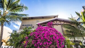 A building with a sign reading "MARINA BEACH" and a vibrant pink bougainvillea in front. - Résidence Marina Beach (Nouméa)