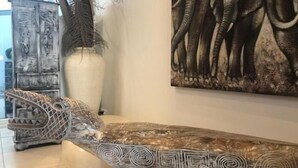 A room with a marble bench, a large painting of elephants, a decorative vase, and a cabinet with carved designs. - Résidence Marina Beach (Nouméa)