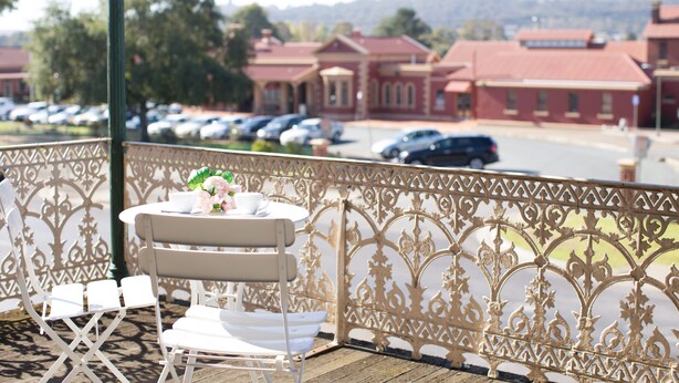A balcony with a table set for two, overlooking a parking area and buildings. - Southern Railway Hotel Goulburn (Goulburn)