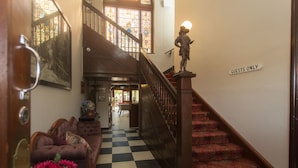 A hotel lobby with a checkered floor, a staircase with a 'GUESTS ONLY' sign, a sofa with a vase of flowers, and a stained glass window. - Southern Railway Hotel Goulburn (Goulburn)
