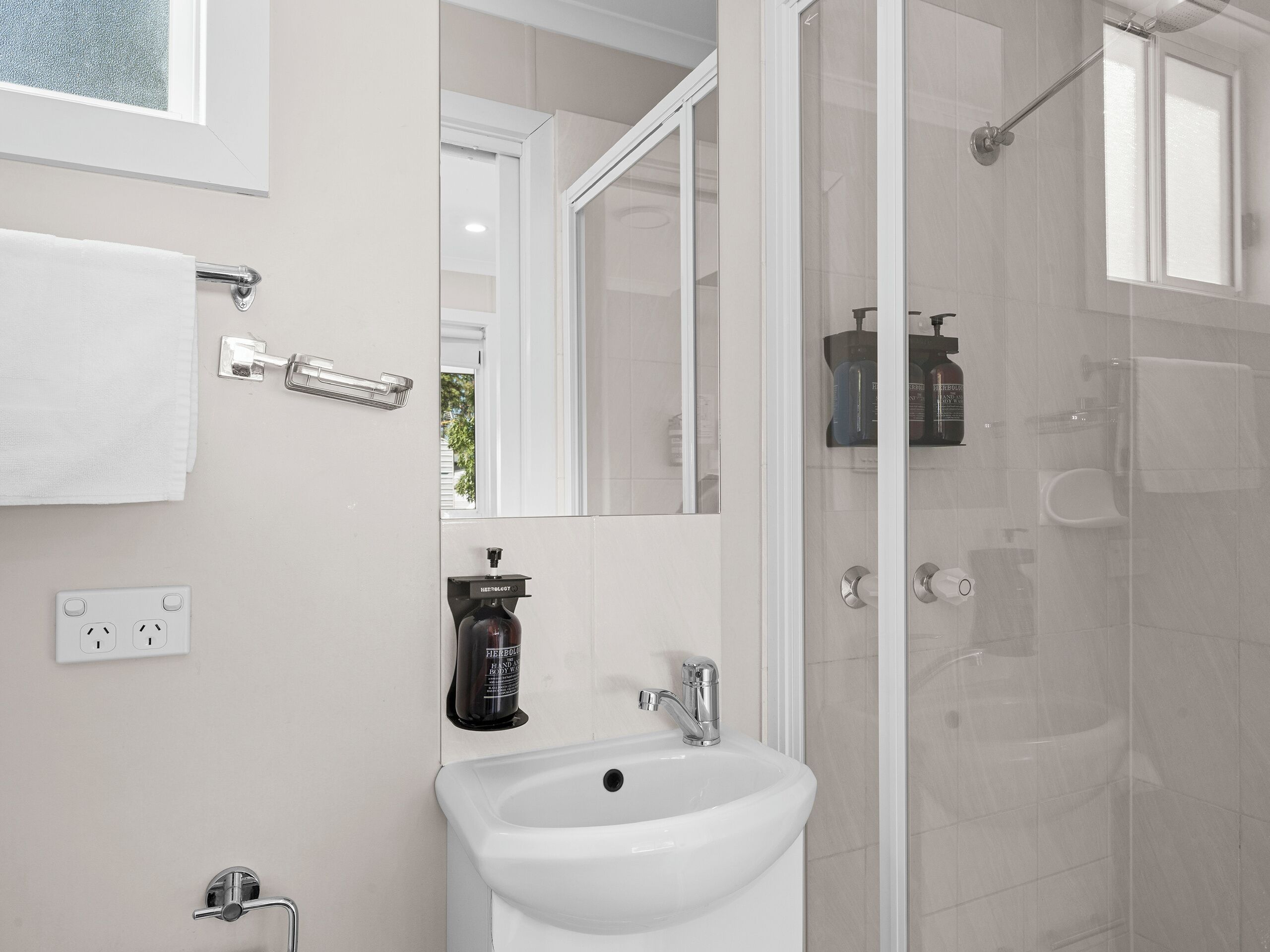 A modern bathroom with a white sink, a glass shower enclosure, and a mirror above the sink.