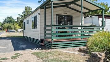 A small, single-story mobile home with a green porch and a covered outdoor seating area.
