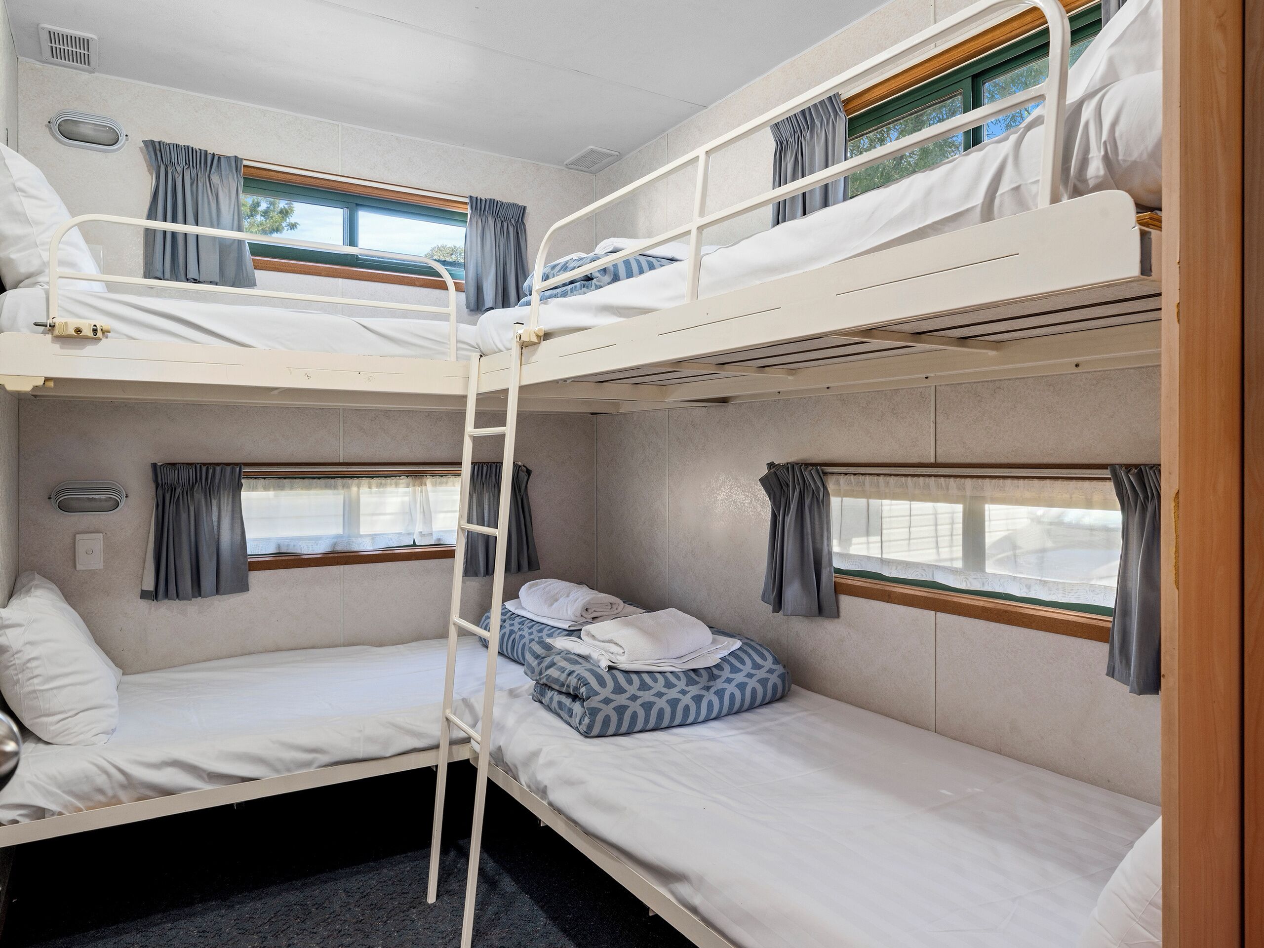 A bunk bed room with a ladder, a window with curtains, and a small bedside table.