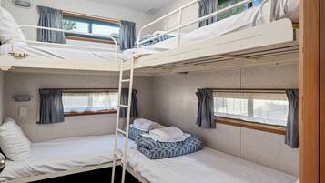 A bunk bed room with a ladder, a window with curtains, and a small bedside table.