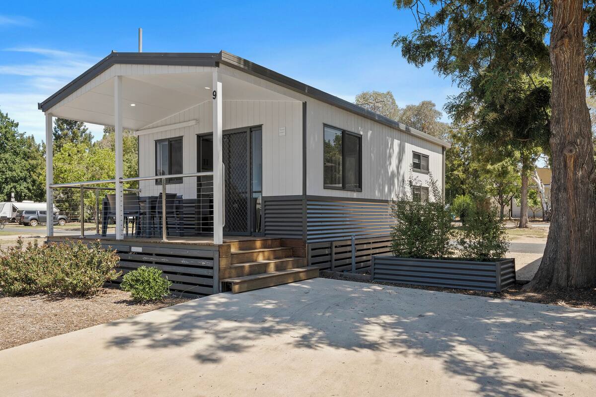 Ein modernes Mobilheim mit überdachter Veranda, großen Fenstern und einer kleinen Terrassenfläche.