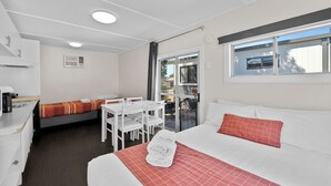 A hotel room with a bed, a small table, and a chair. There is a window with a view of the outside. - Wodonga Holiday Park (West Wodonga)